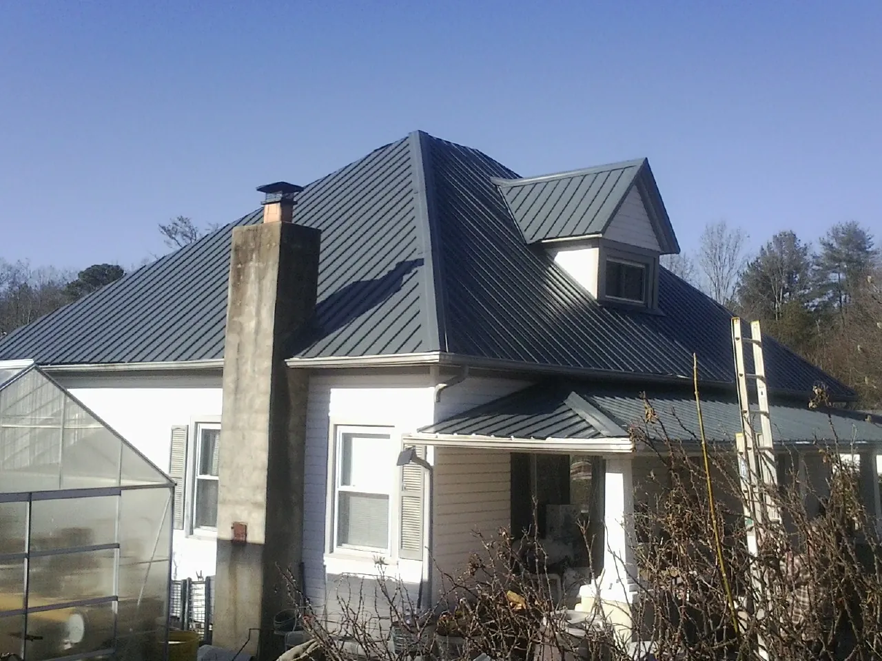 Dark blue standing seam metal roof on a white farmhouse with dormer — Slate & Tile Roof Repair by Roofing Brothers in Todd