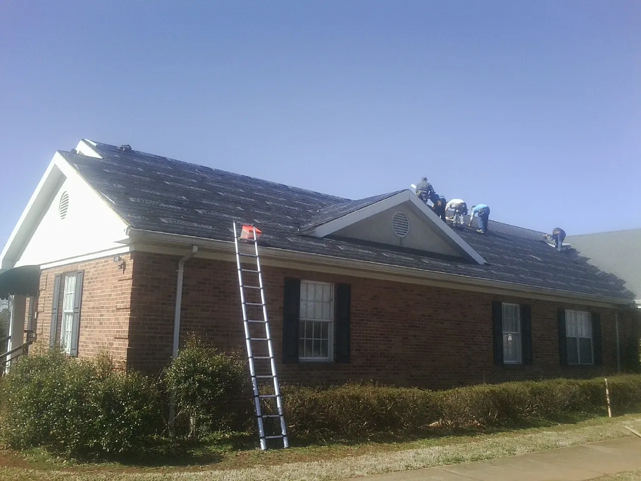 Crew tearing shingles off a brick ranch roof with a ladder set — Metal Roof Repair work by our crew in Todd