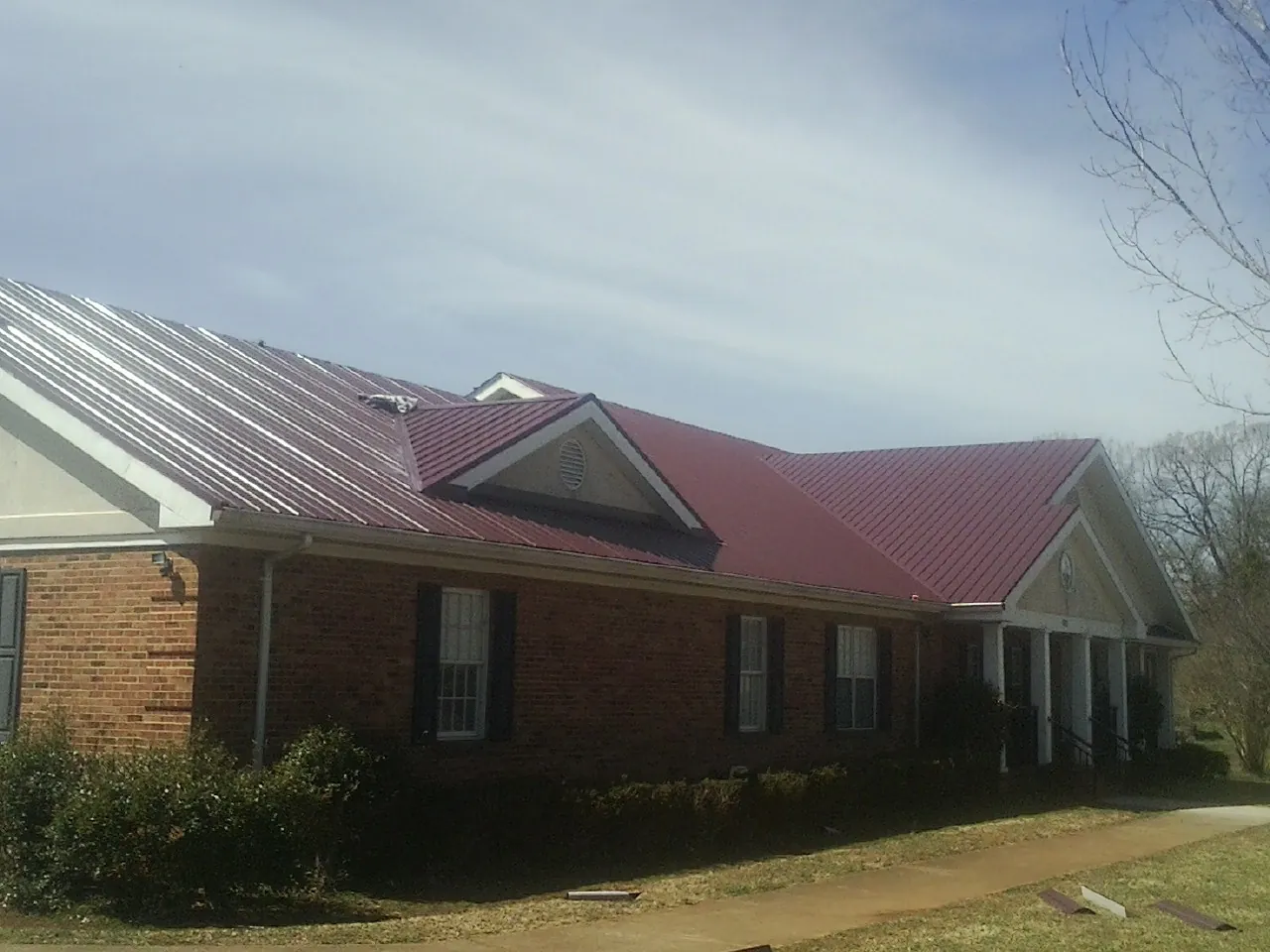 Red metal roof with gabled entries on a long brick building, from a Hail Damage Roof Repair job in Todd