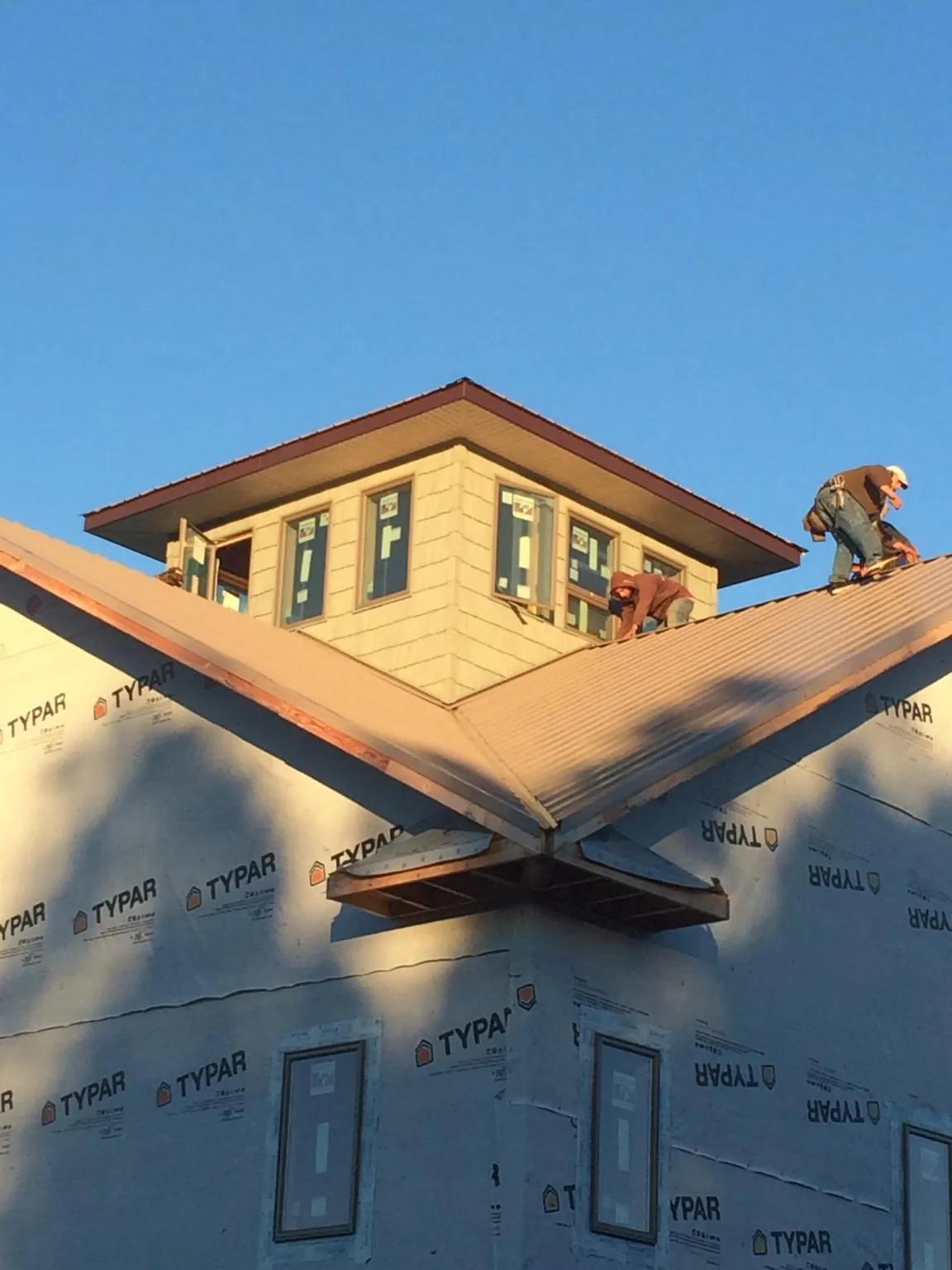 Roofers working around a rooftop cupola on a new metal roof at sunset — Roof Waterproofing in Todd by Roofing Brothers